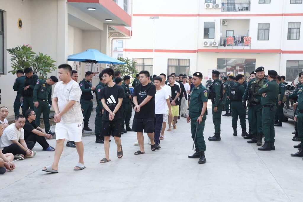 Armed Cambodian police secure the premises while suspects are ordered to remain seated during the coordinated enforcement action involving nearly 700 officers.